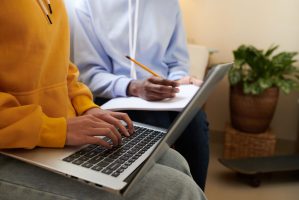 Hands of female college student coding on laptop when her friend drawing wibsite wireframe in notepad